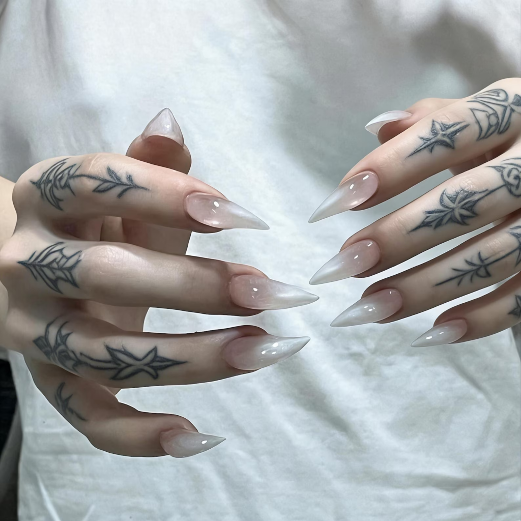 Tattoo hand wearing nude ombre clear tip stiletto press on nails, long pointed gradient false nails aesthetic manicure