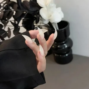 Aesthetic hand shot milky white sheer extra long stiletto press on nails, translucent sharp pointed fake nails dark floral decor background