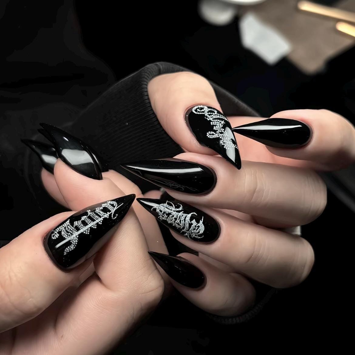 Hands wearing handmade black stiletto press on nails with silver graffiti art