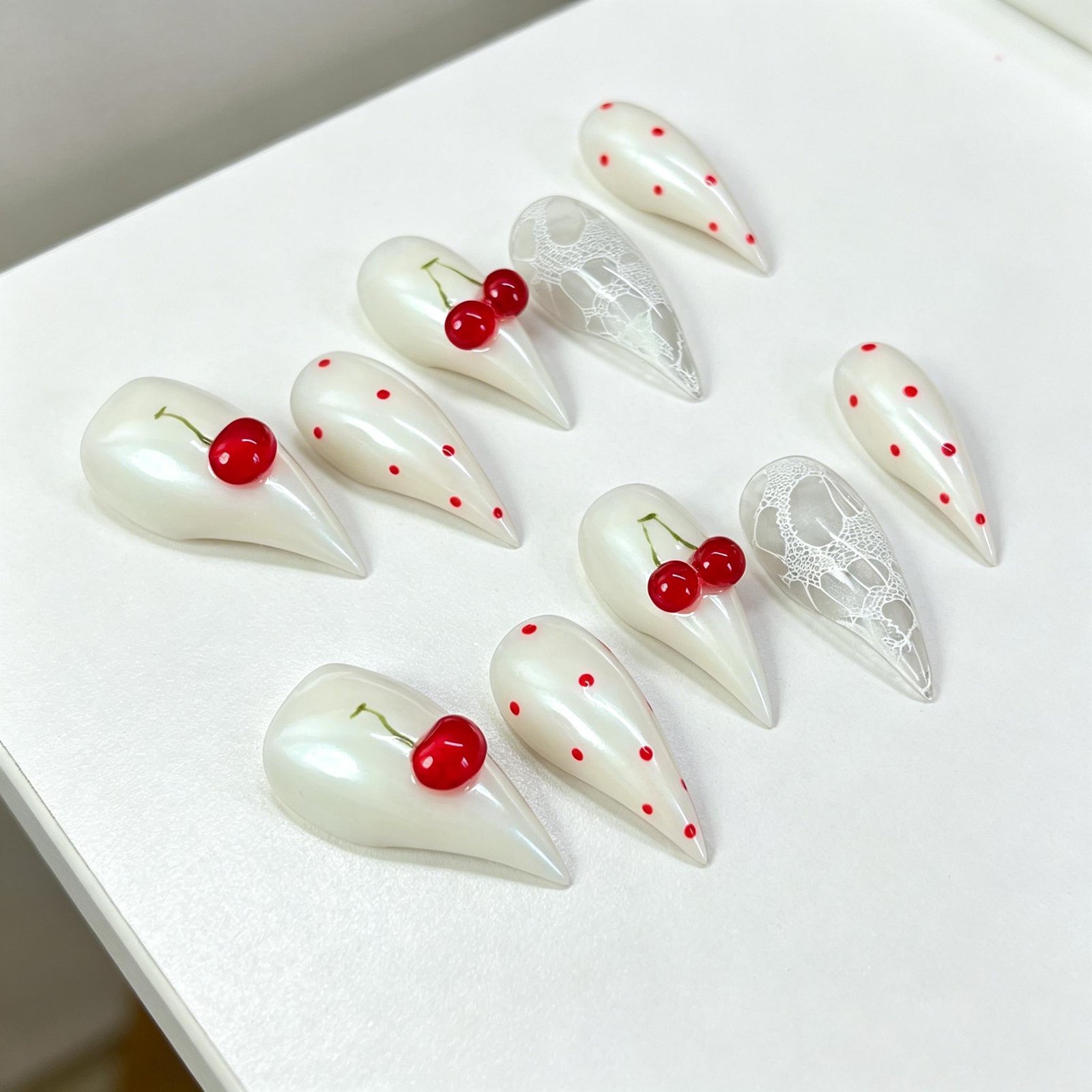 Angled flat lay of cherry milky white stiletto press on nails with 3D cherry charms and sheer clear nails