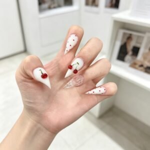 Hand wearing handmade milky white stiletto press on nails with 3D cherry charms and tiny red polka dots