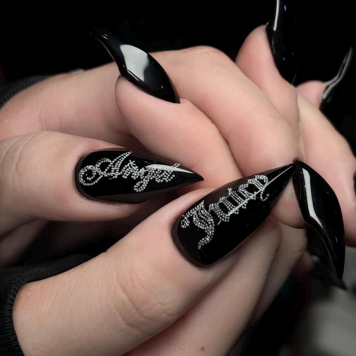 Extreme closeup of long black stiletto press on nails with silver graffiti letter design