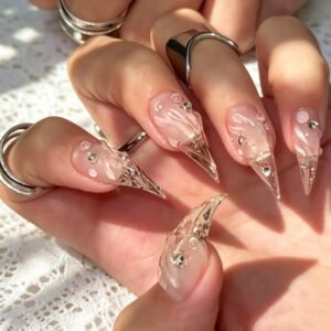 Glossy nude stiletto press-on nails with silver jewelry-inspired nail art and rhinestones