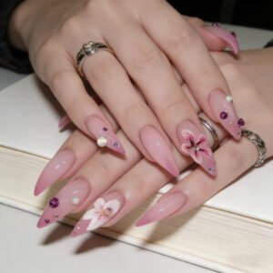 Hands wearing matte pink stiletto press on nails with hand-painted floral art and tiny crystal studs