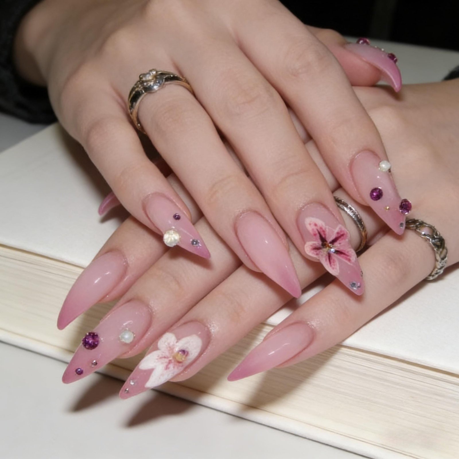 Hands wearing matte pink stiletto press on nails with hand-painted floral art and tiny crystal studs