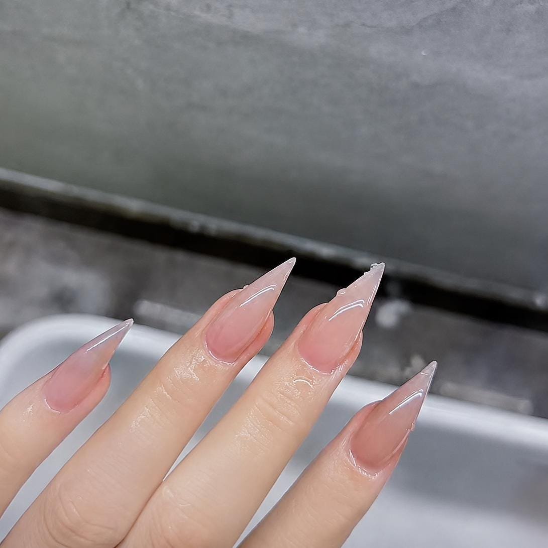 Angled shot of hands fitted with nude pink sheer french tip stiletto press on nails