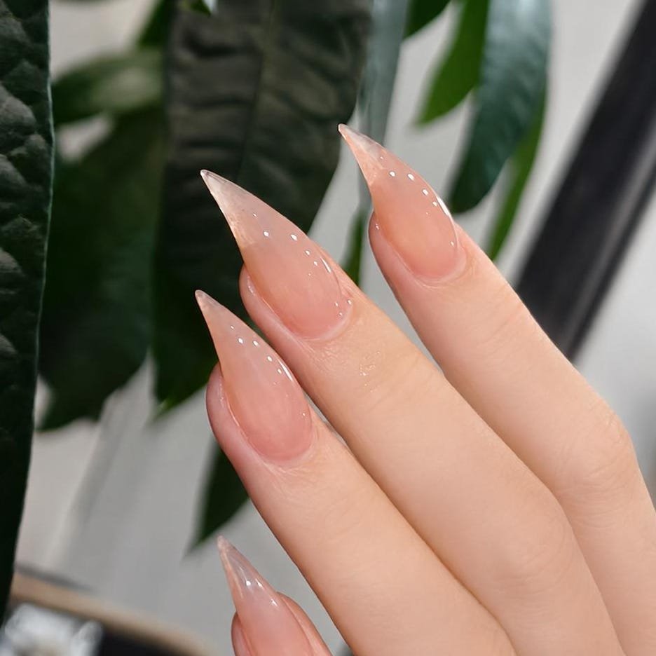 Hands wearing matte nude pink stiletto press on nails with sheer white french tips