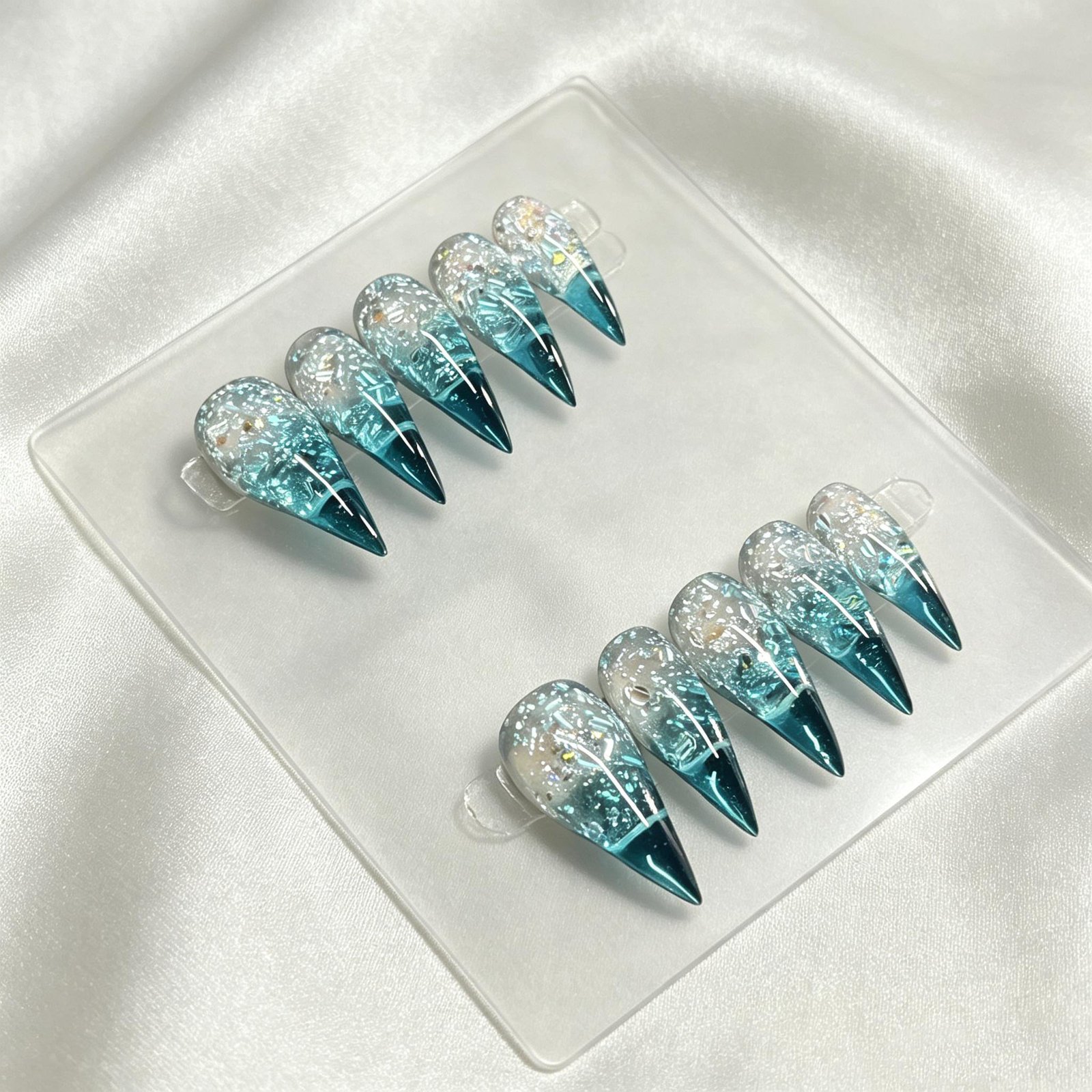 Handmade blue iridescent foil stiletto press on nails laid flat on white silk fabric