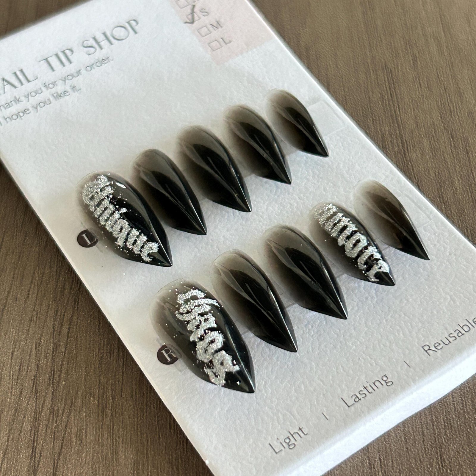 Black stiletto press on nails with silver graffiti design laid flat on display tray