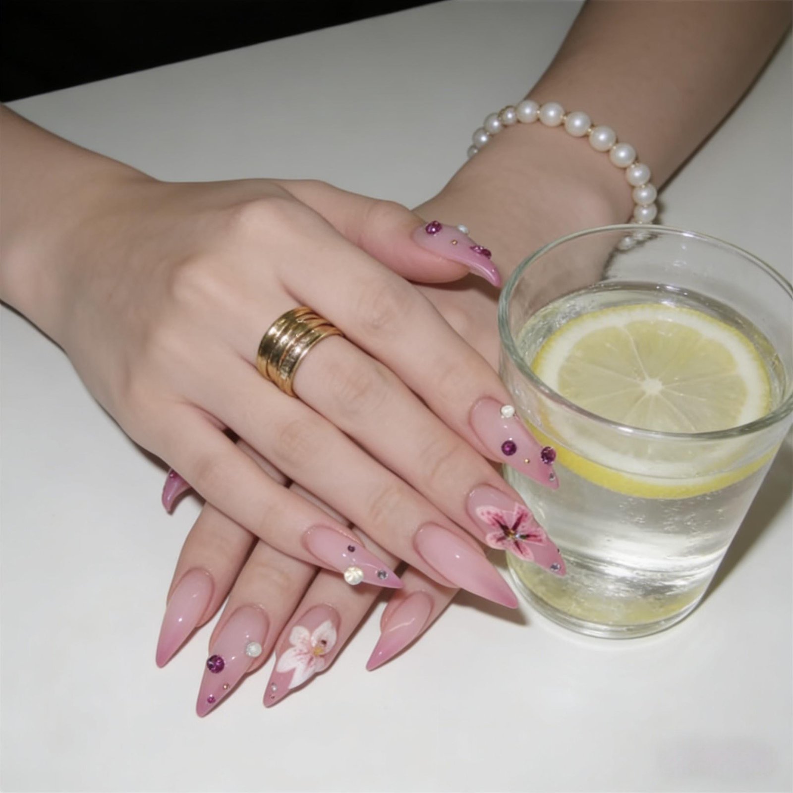 Model hands with pink floral stiletto press on nails placed beside lemon water glass