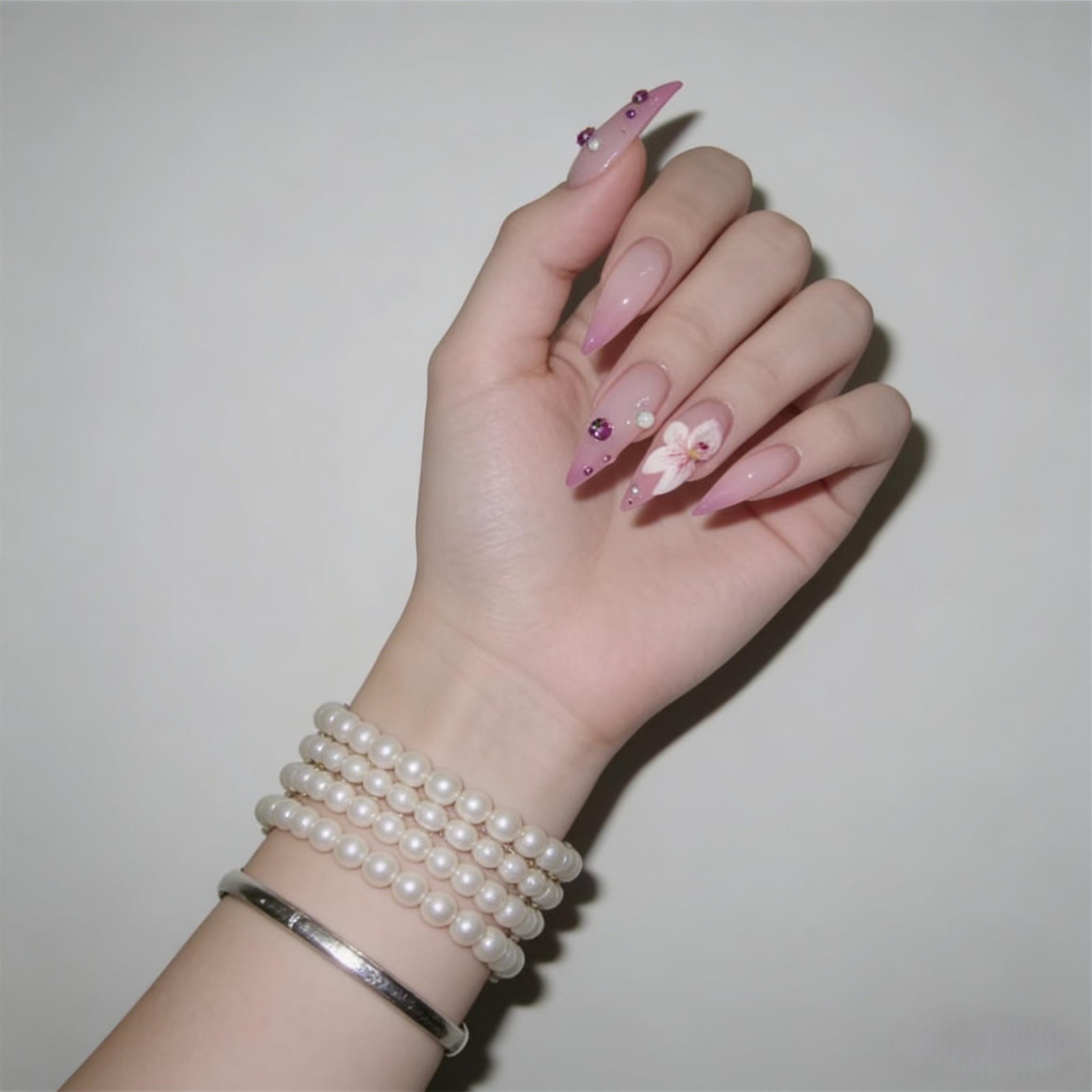 Single hand angled view with pink floral stiletto press on nails and pearl bracelets