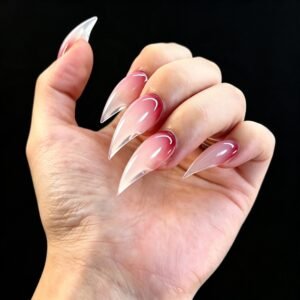 Tilted palm view blush pink gradient stiletto press on nails, sheer clear long pointed ombre fake nails studio black backdrop